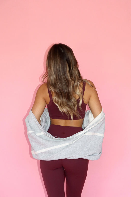 Woman wearing a grey warm up shrug over burgundy activewear shown from behind