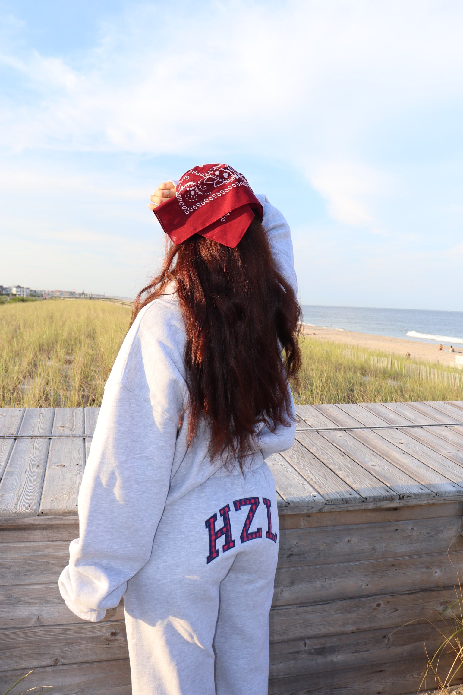 Back view of a woman wearing gray joggers and a matching sweatshirt on a beach boardwalk