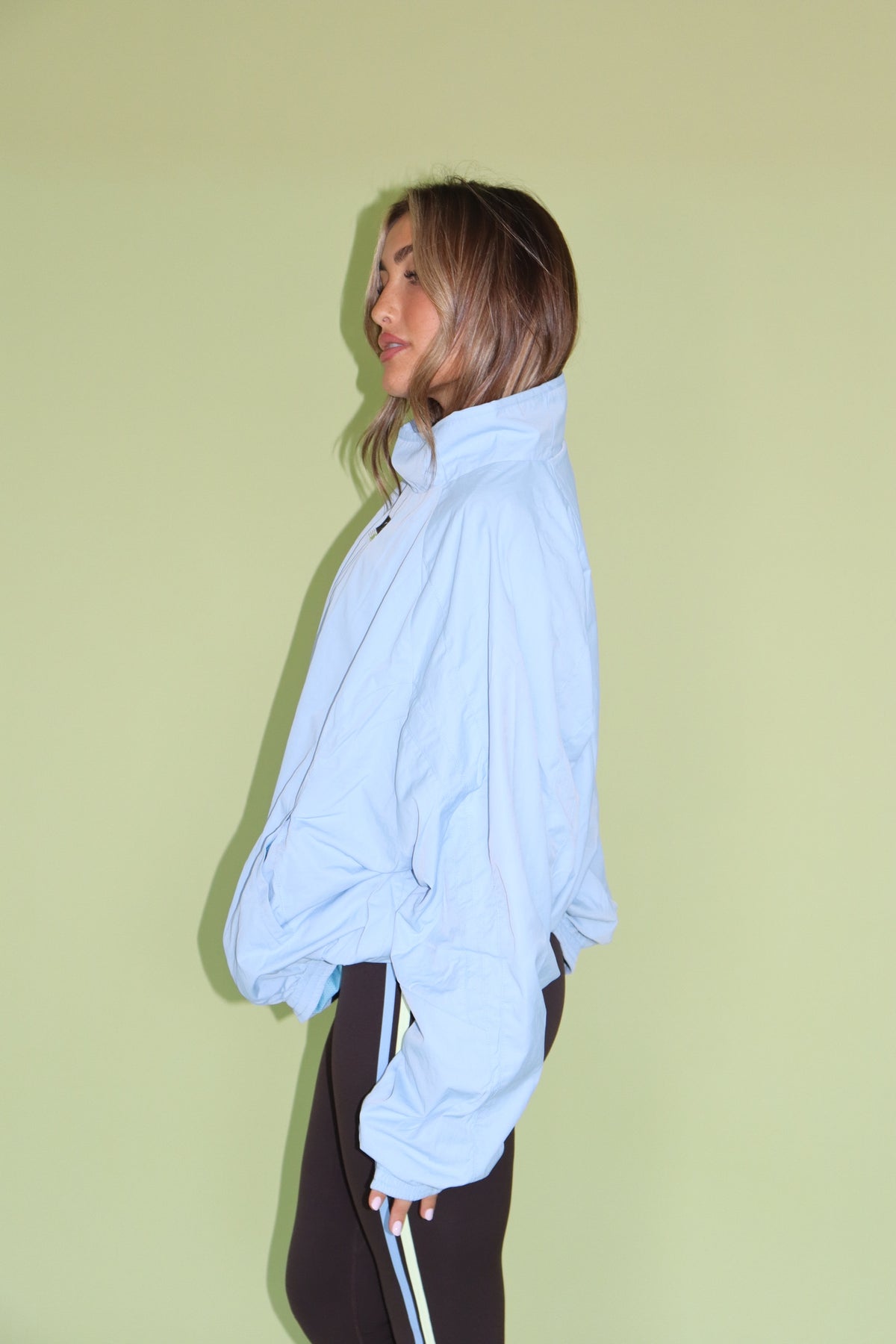 Woman modeling a light blue sport windbreaker with a high collar and relaxed fit over black pants