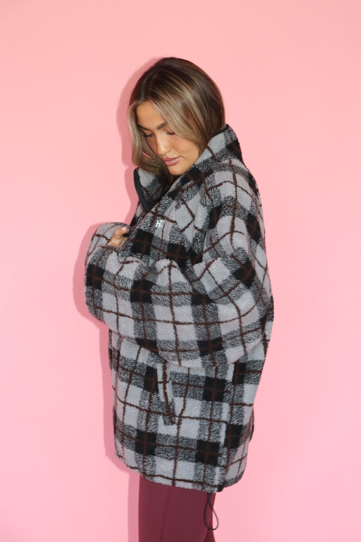 Woman wearing a gray and black plaid hooded fleece jacket against a pink background