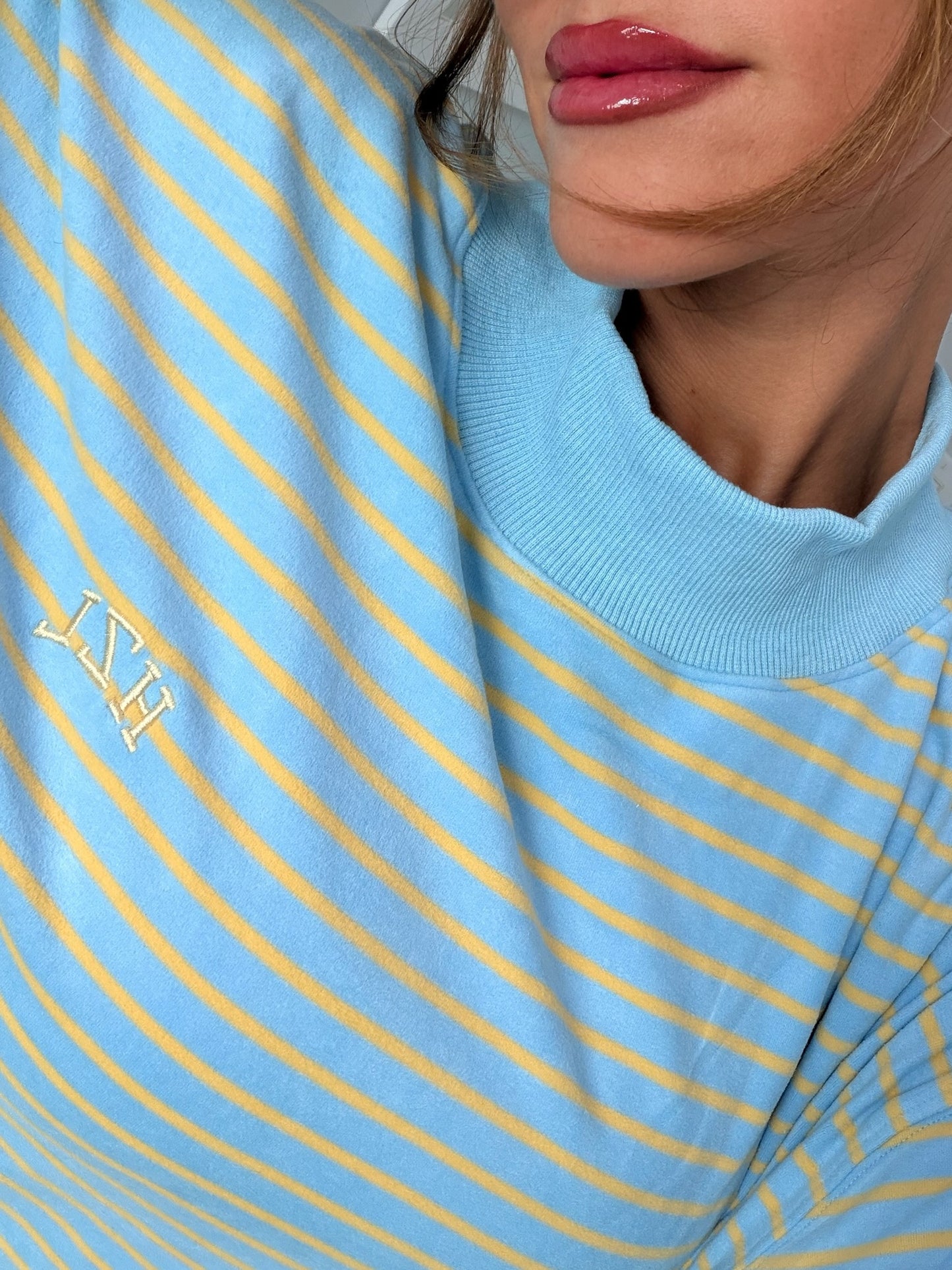 Close-up of a woman wearing a light blue and yellow striped mockneck top with subtle embroidered detailing, styled casually.