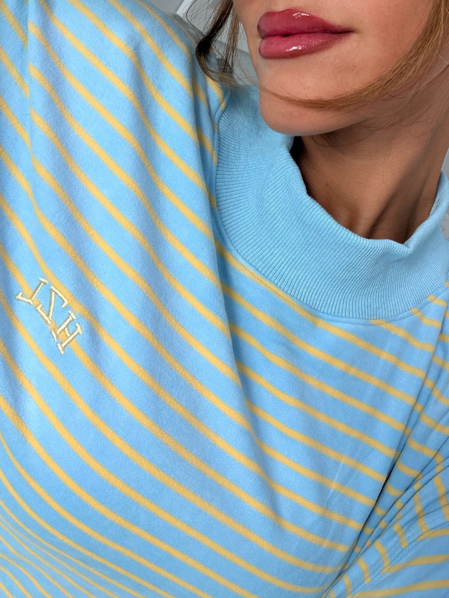 Close-up of a woman wearing a light blue and yellow striped mockneck top with subtle embroidered detailing, styled casually.