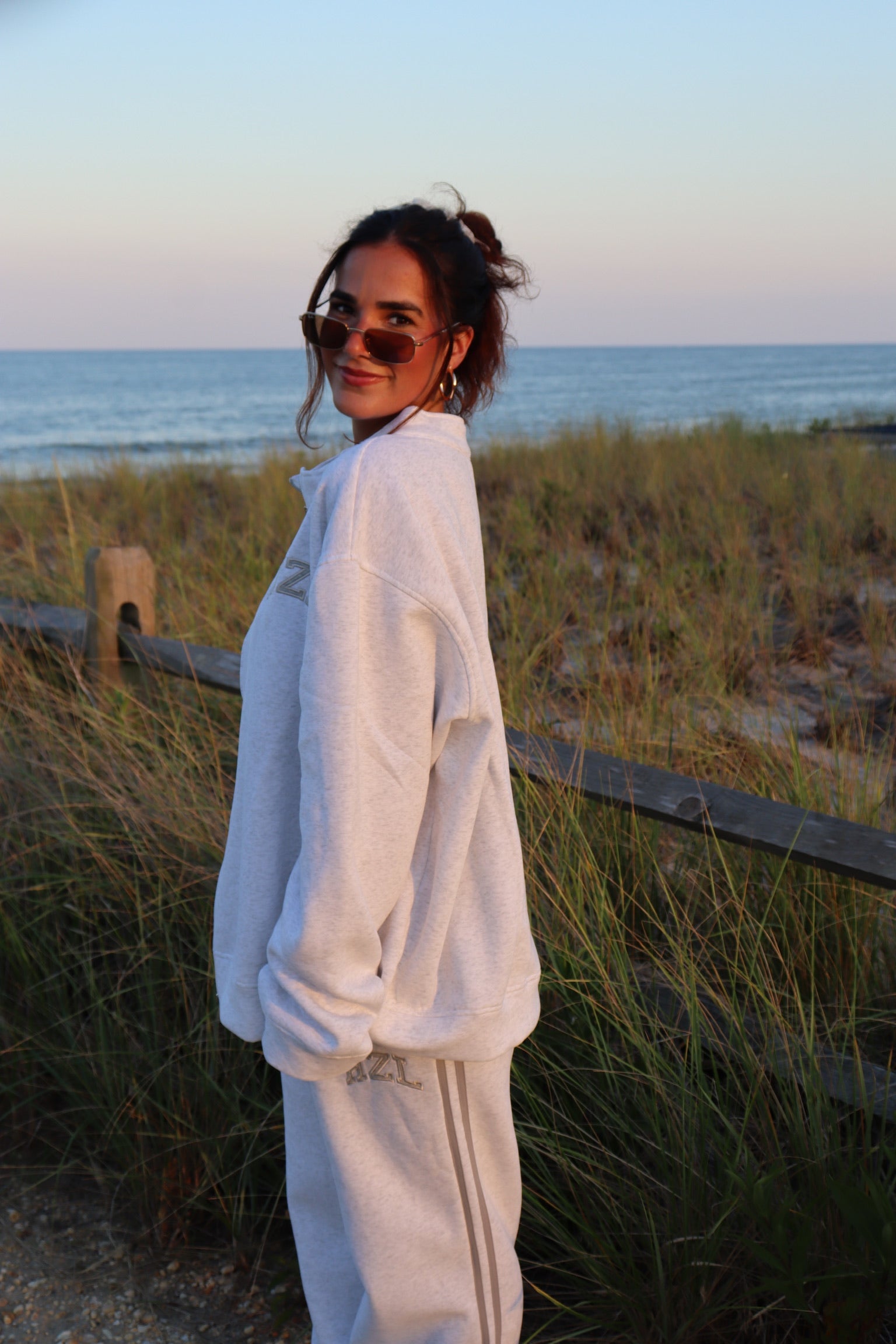 Woman wearing an oversized cream zip-up sweatshirt and matching pants beside beach dunes