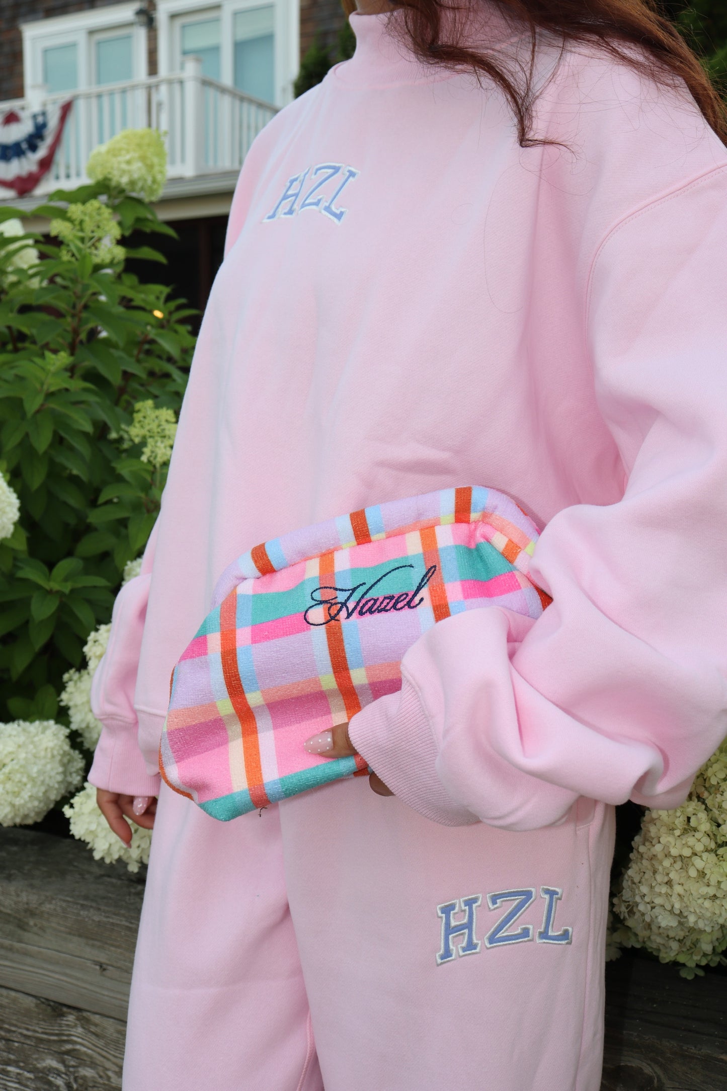 Pink HZL mockneck sweatshirt and matching pants with a colorful plaid pouch outdoors