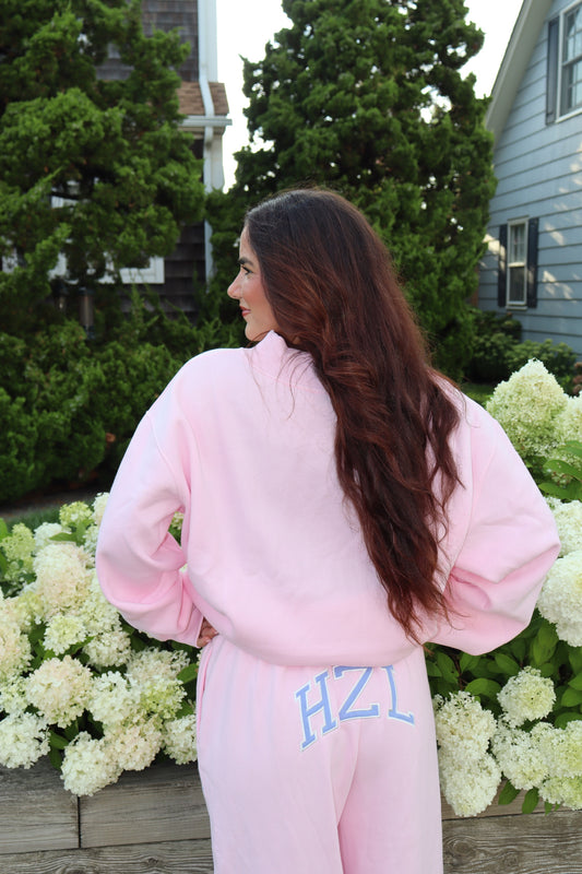Woman modeling pink HZL sweatpants in a garden filled with white hydrangeas