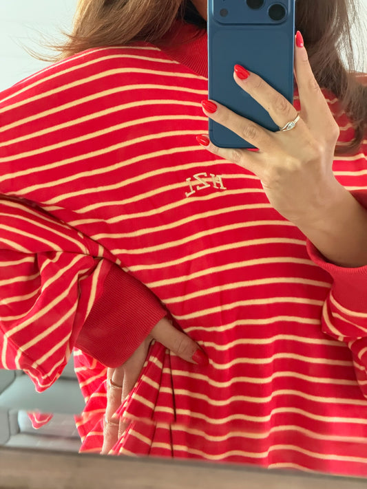 Close-up of a person wearing a red and cream striped mockneck sweater with embroidered detailing, holding a phone with painted red nails.