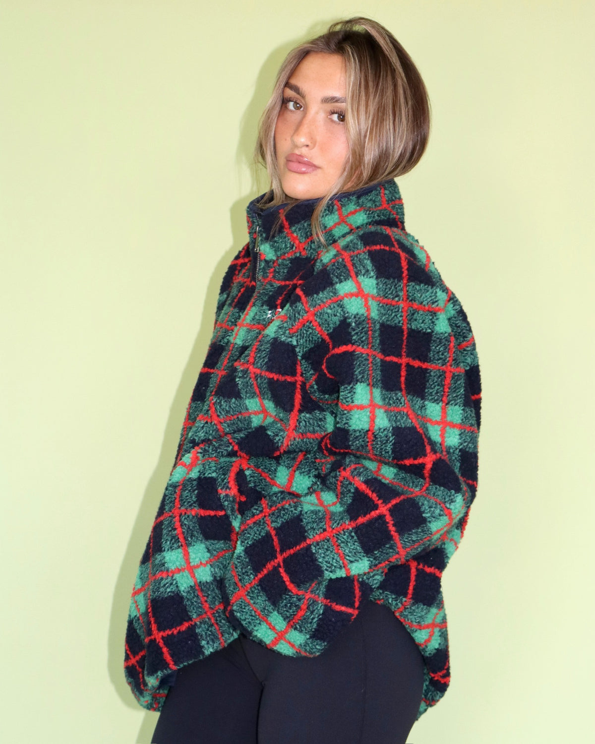 Woman wearing a green red and navy plaid fleece mockneck pullover against a pale green background