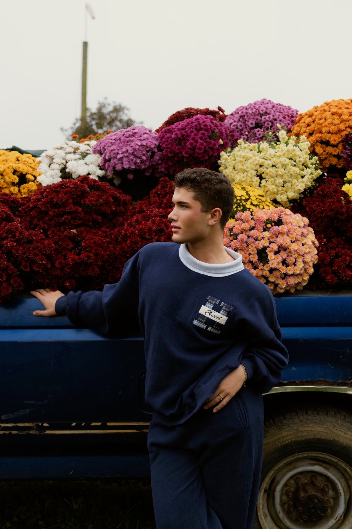 Model wearing a navy HZL mockneck sweatshirt and matching pants beside a colorful flower truck