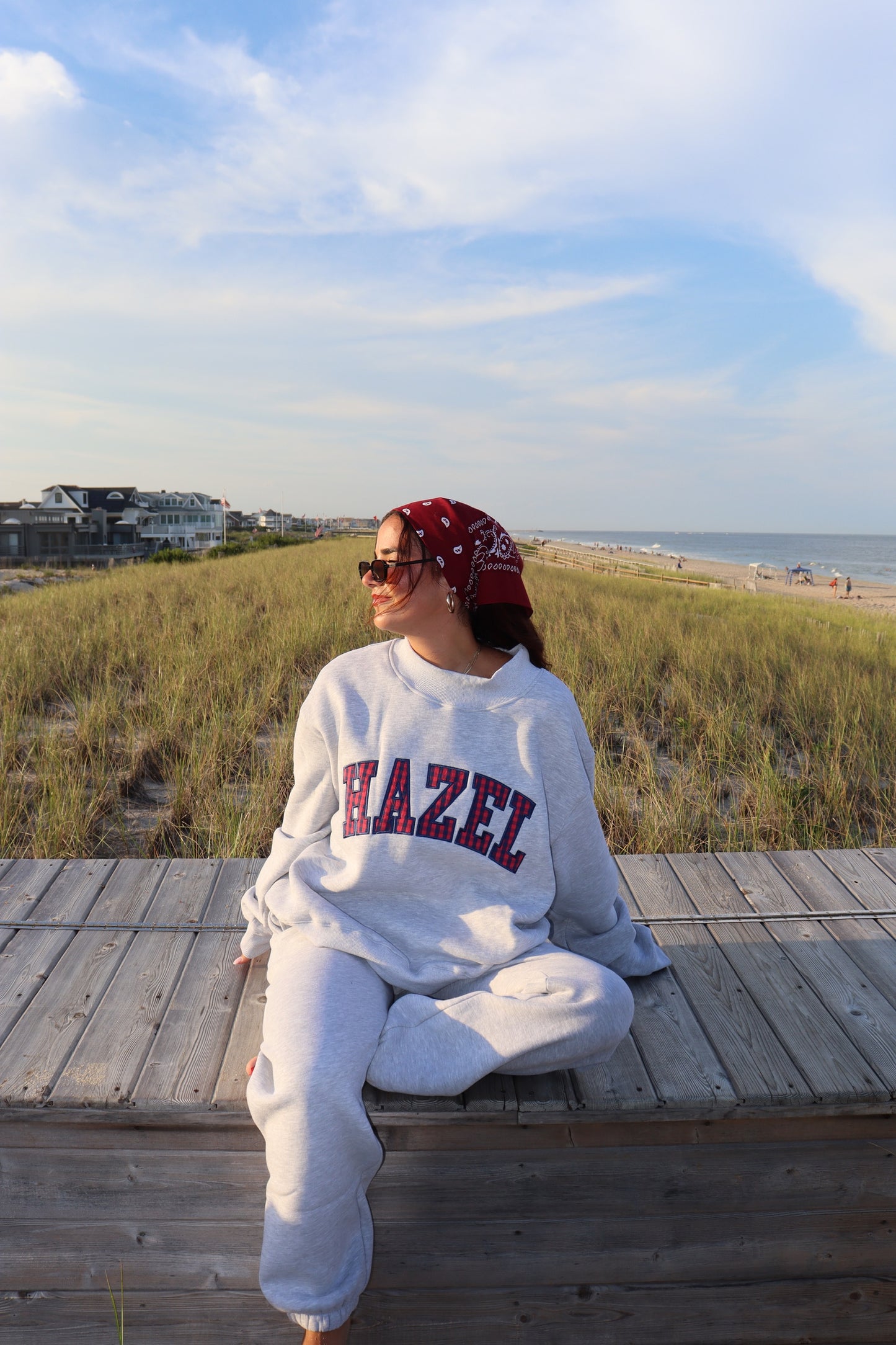 Woman wearing gray HZL joggers and matching sweatshirt seated on a beach boardwalk in coastal dunes