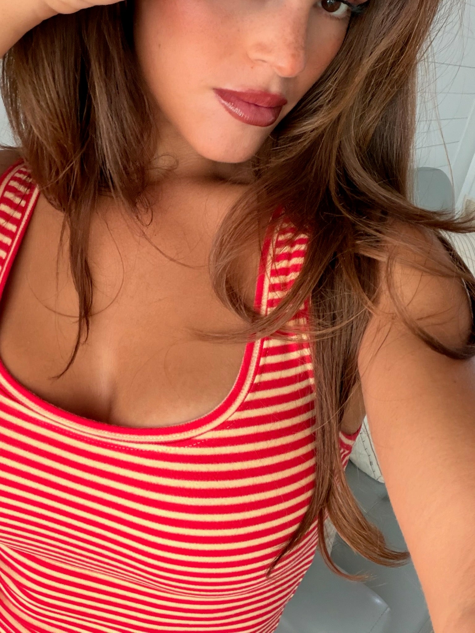 Close-up of a woman wearing a red and white striped tank top with natural makeup and loose hair, casual summer look.