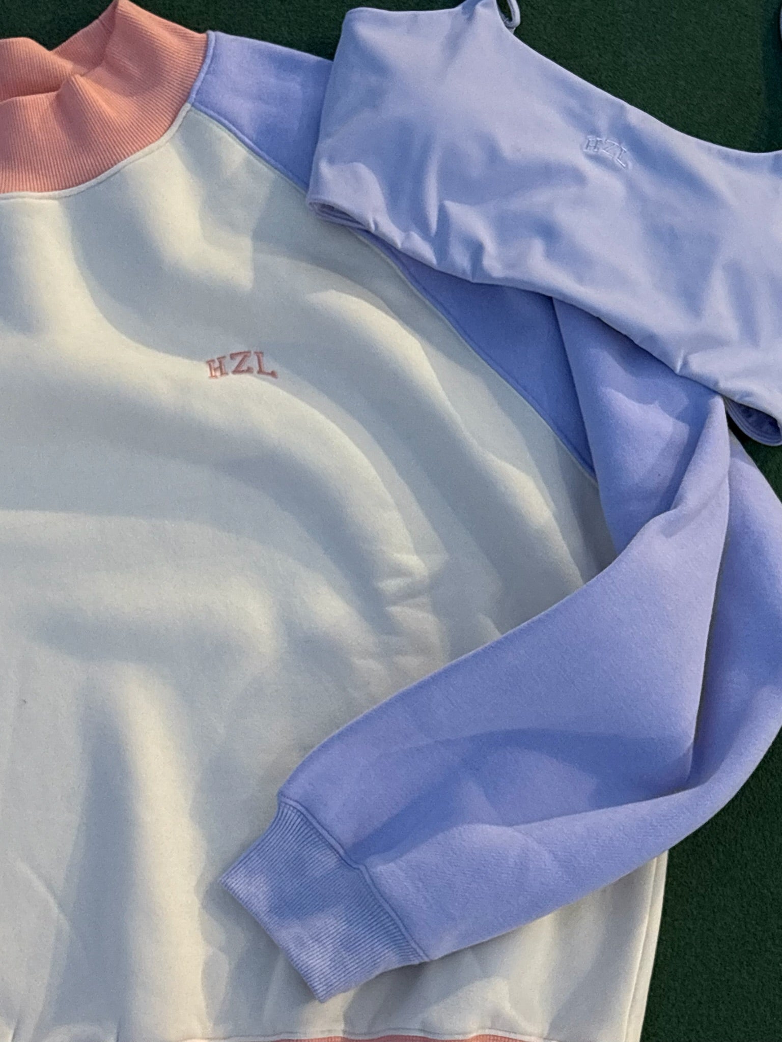 Close-up of pastel color-blocked sweatshirt with pink mockneck collar and embroidered hzl logo on chest and sleeve