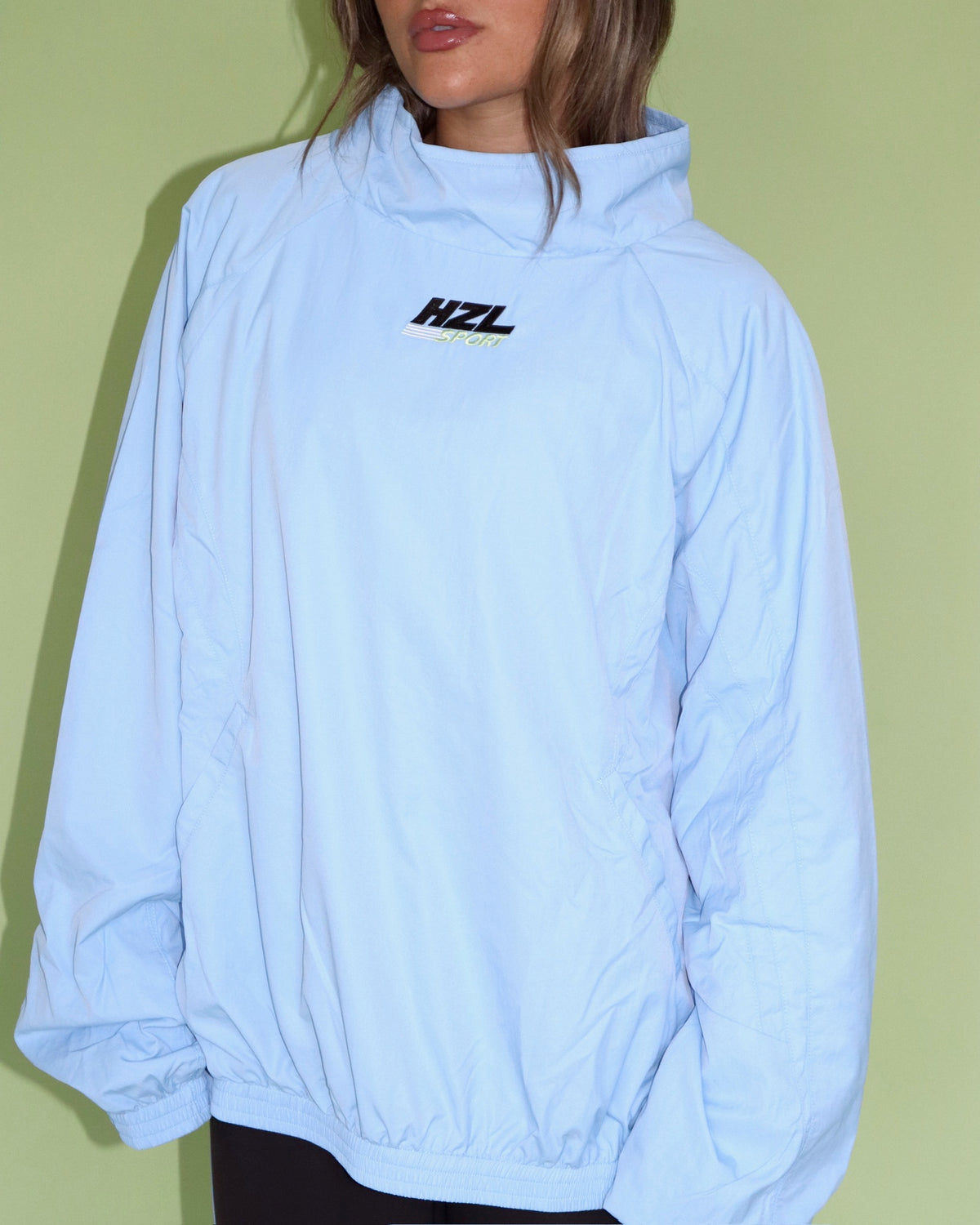 Model wearing a light blue HZL windbreaker with a hood and elastic cuffs