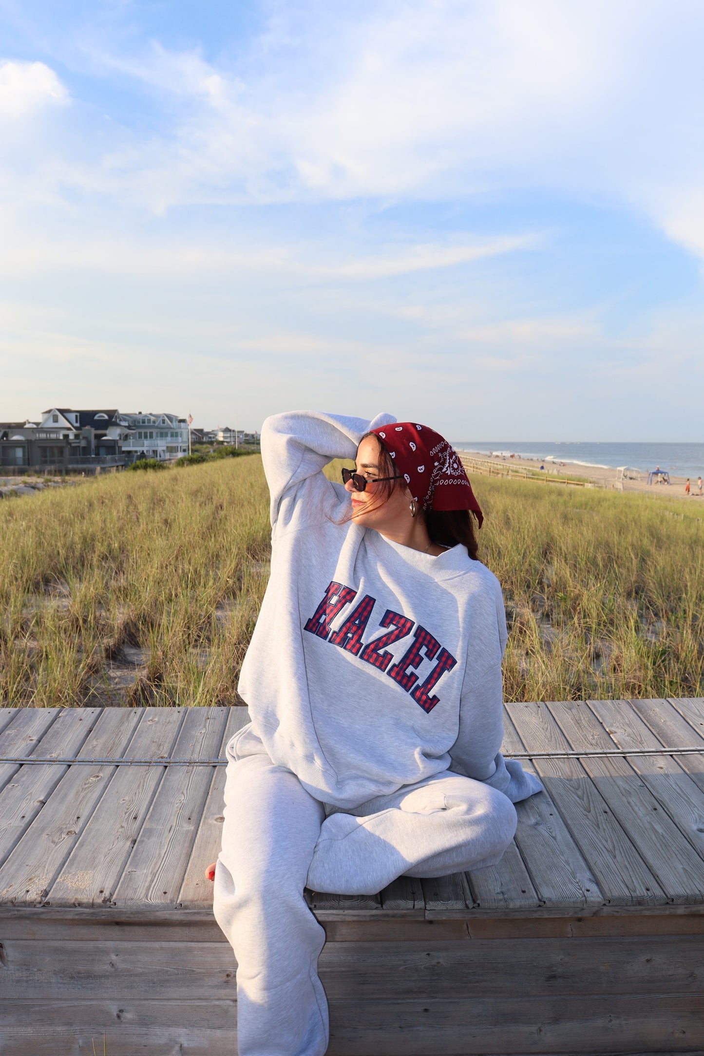 Person wearing a light gray mockneck sweatshirt and matching pants on a beach boardwalk beside the dunes
