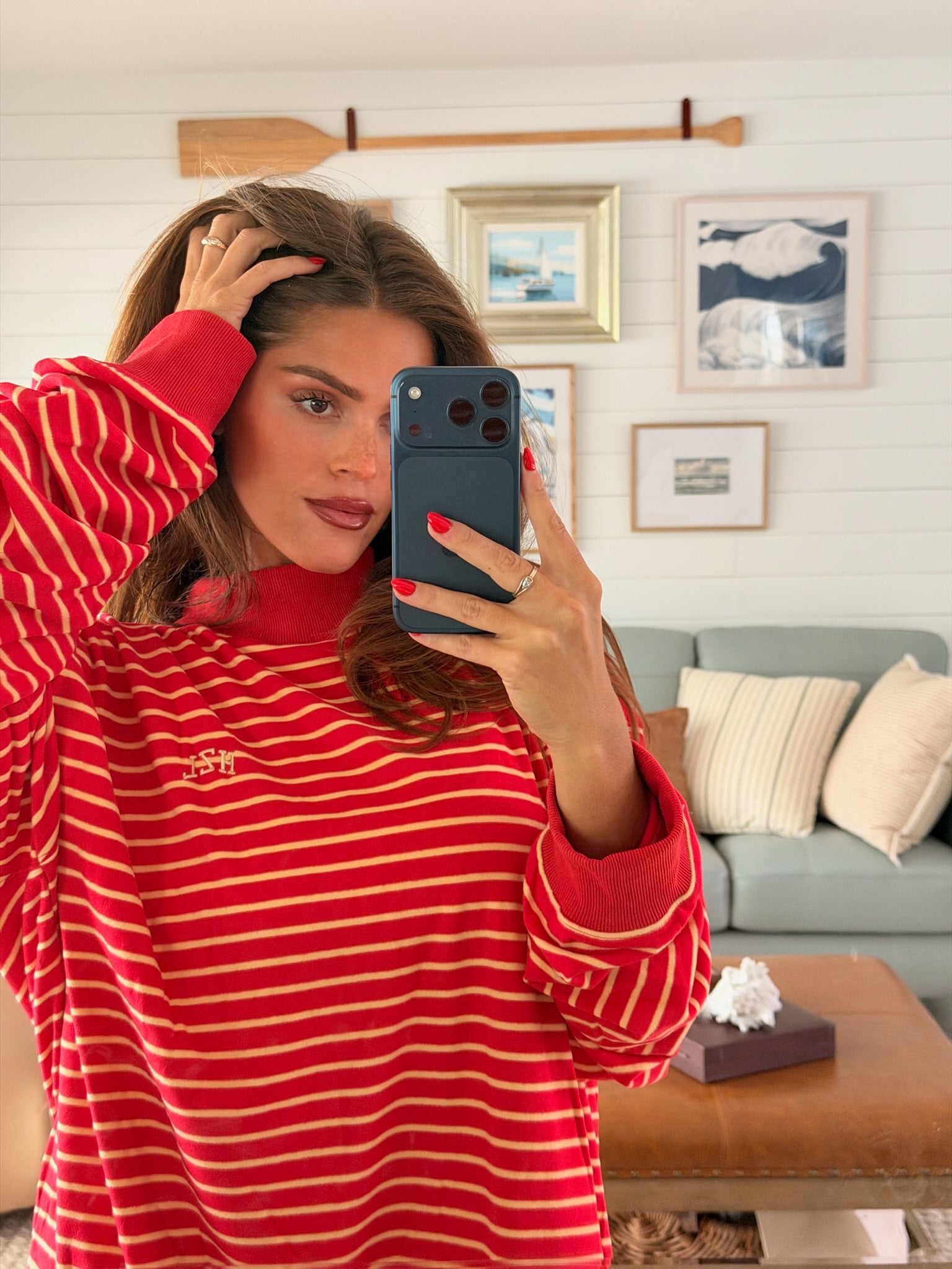 Woman taking a mirror selfie wearing a red and yellow striped mockneck sweater with casual living room decor in the background