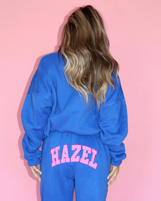 Back view of a model wearing bright blue joggers with pink HAZEL lettering on the back waistband