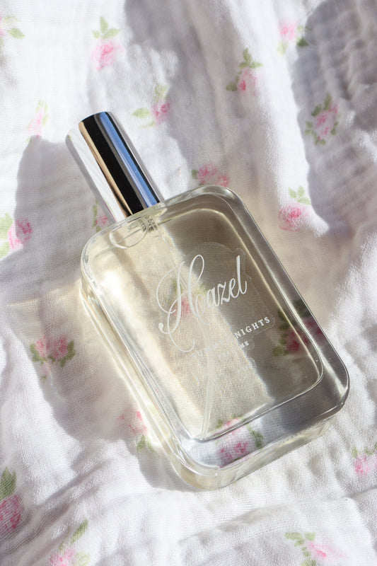 Hazel Summer Nights perfume bottle resting on floral white fabric in soft sunlight