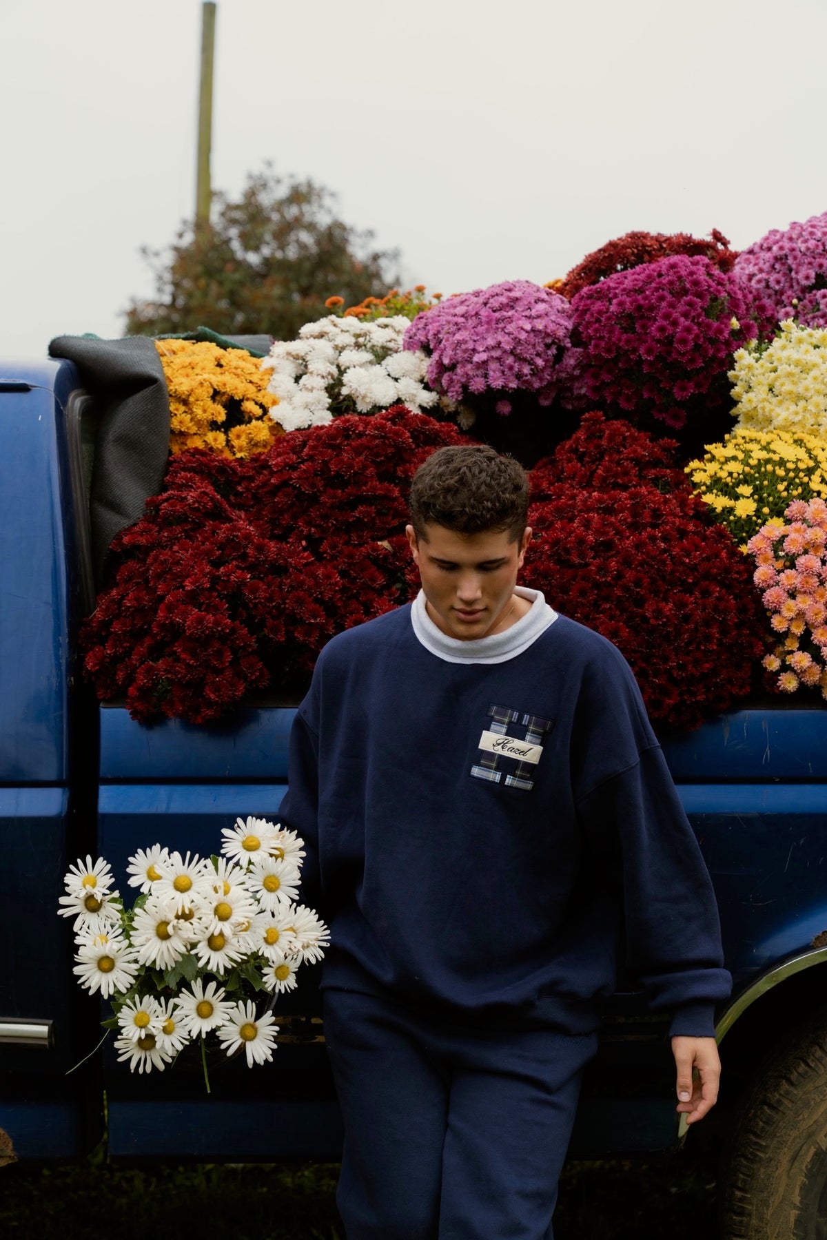 Man wearing a navy mockneck sweatshirt beside a flower filled blue truck