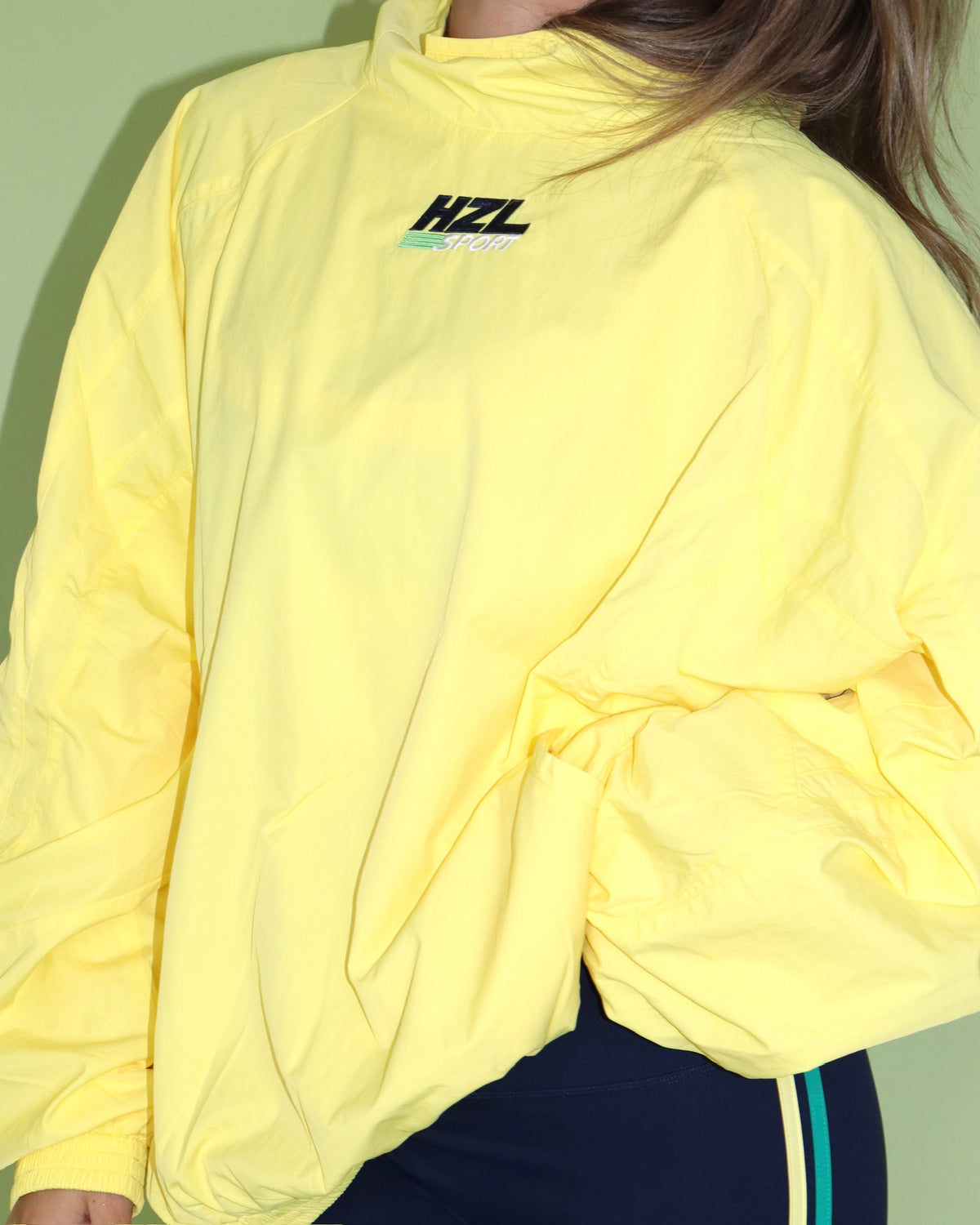 Yellow HZL Sport jacket with mock neck and cinched waist worn with navy track pants