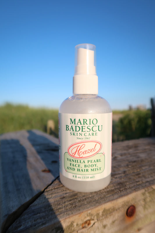 Clear spray bottle of vanilla pearl face, body, and hair mist on wooden surface outdoors with blue sky background