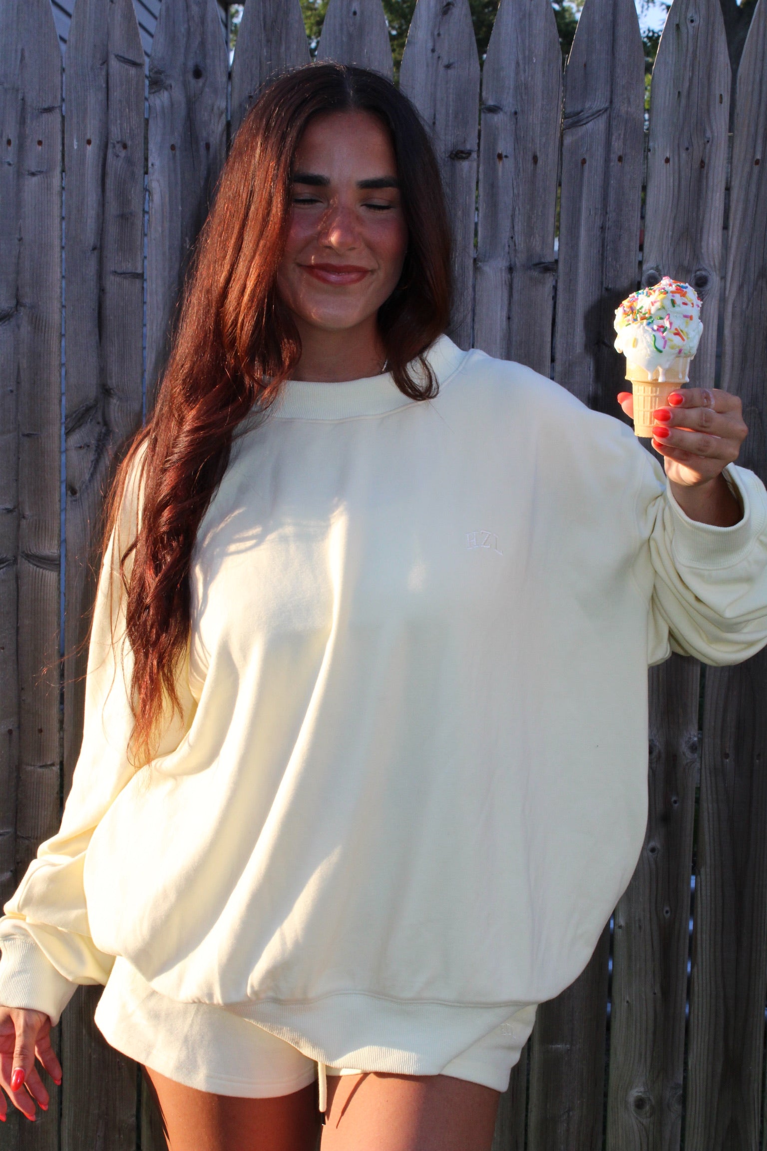 Woman wearing a relaxed banana-yellow mockneck sweatshirt and matching shorts holding an ice cream cone with sprinkles outdoors