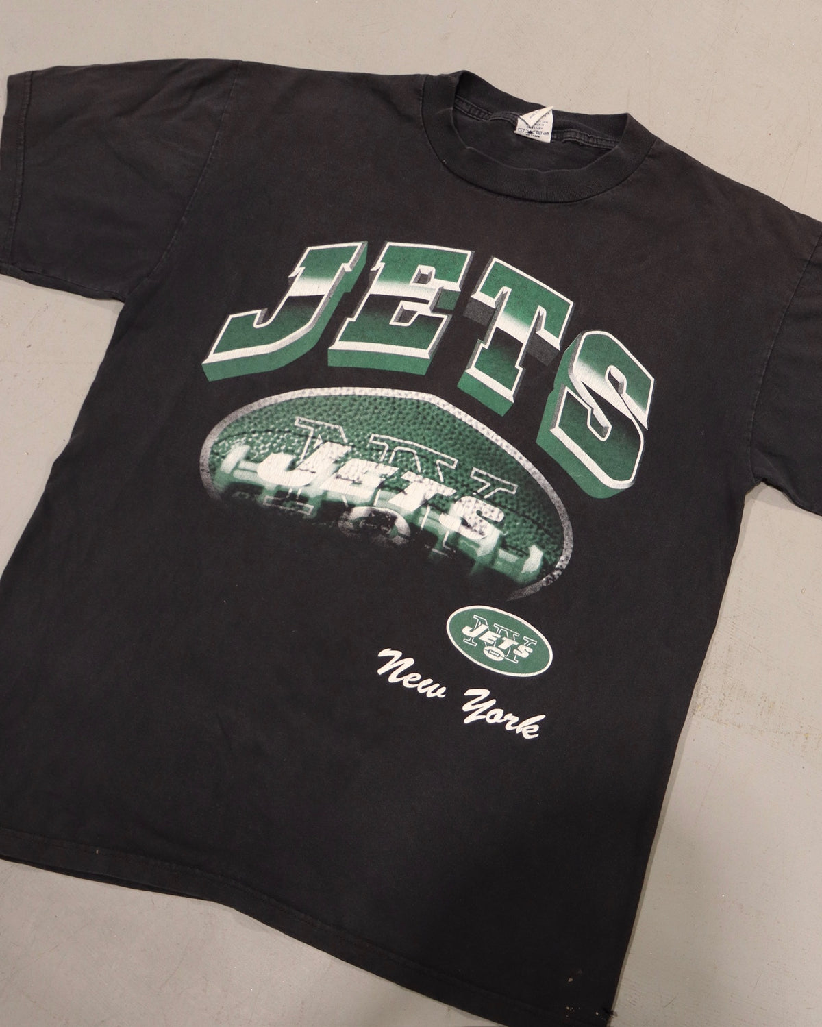 Black vintage New York Jets tee with green and white lettering and football helmet graphic laid flat