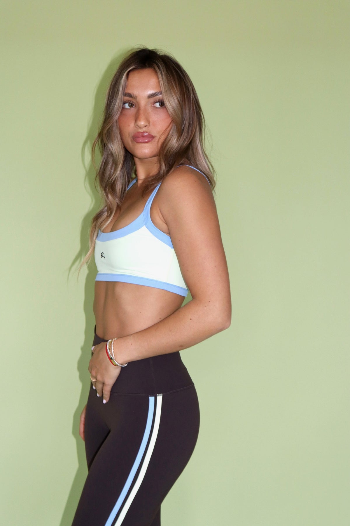 Model wearing a brown and white athletic bra with blue trim and matching leggings against a green backdrop