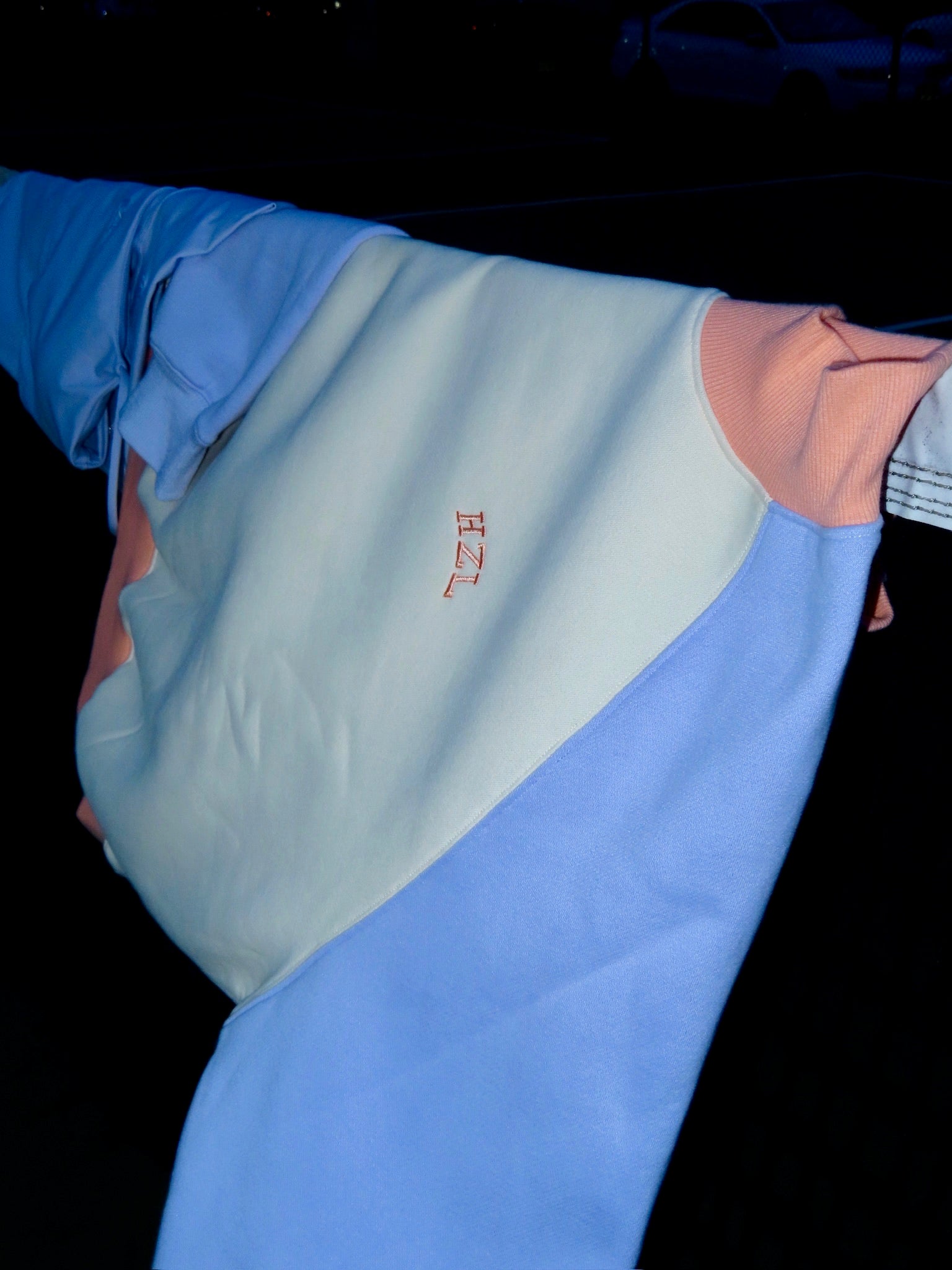 Close-up of a pastel color-blocked sweatshirt with a small embroidered detail hanging outdoors at night.
