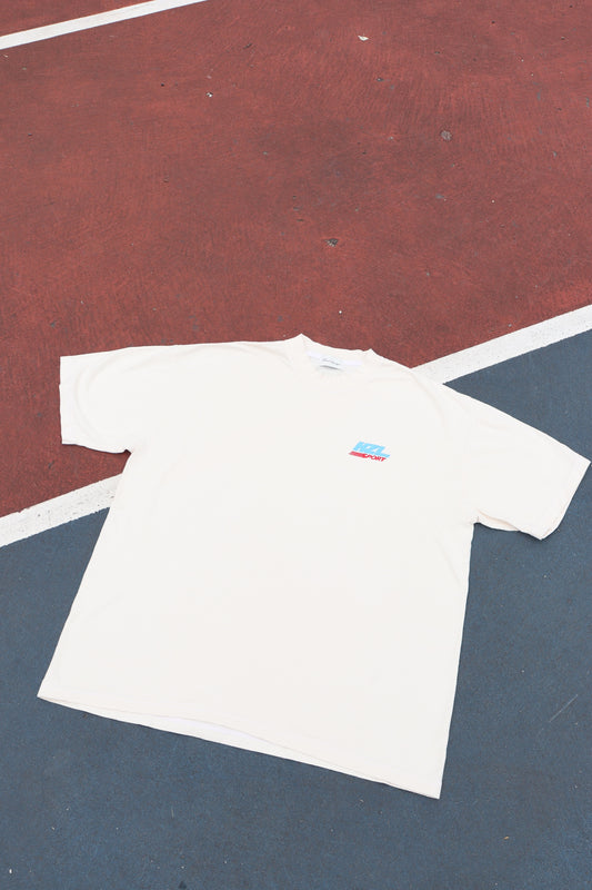 Cream short sleeve tee laid flat on a red and blue court with a small colorful chest graphic