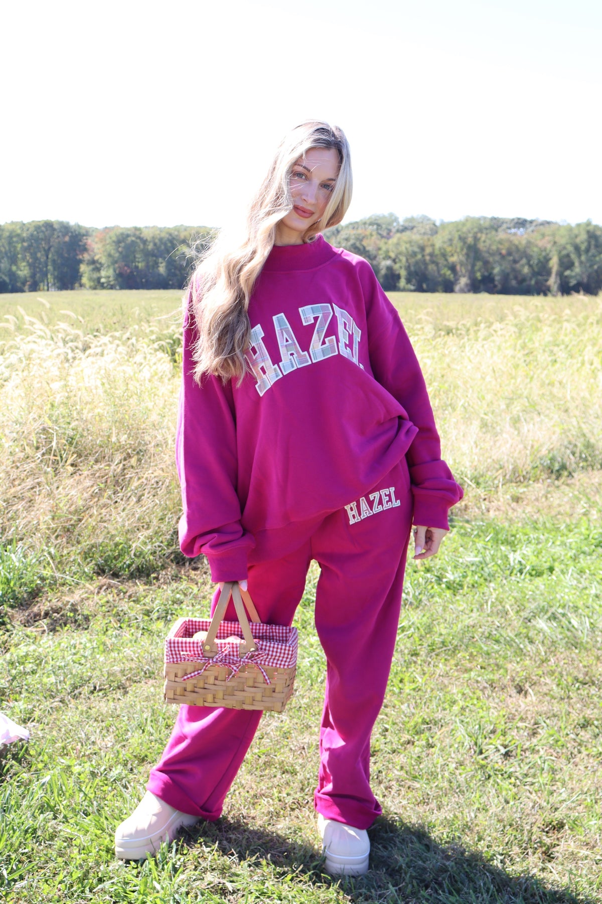 Model wearing a magenta HZL mockneck sweatshirt and matching joggers in a sunny field