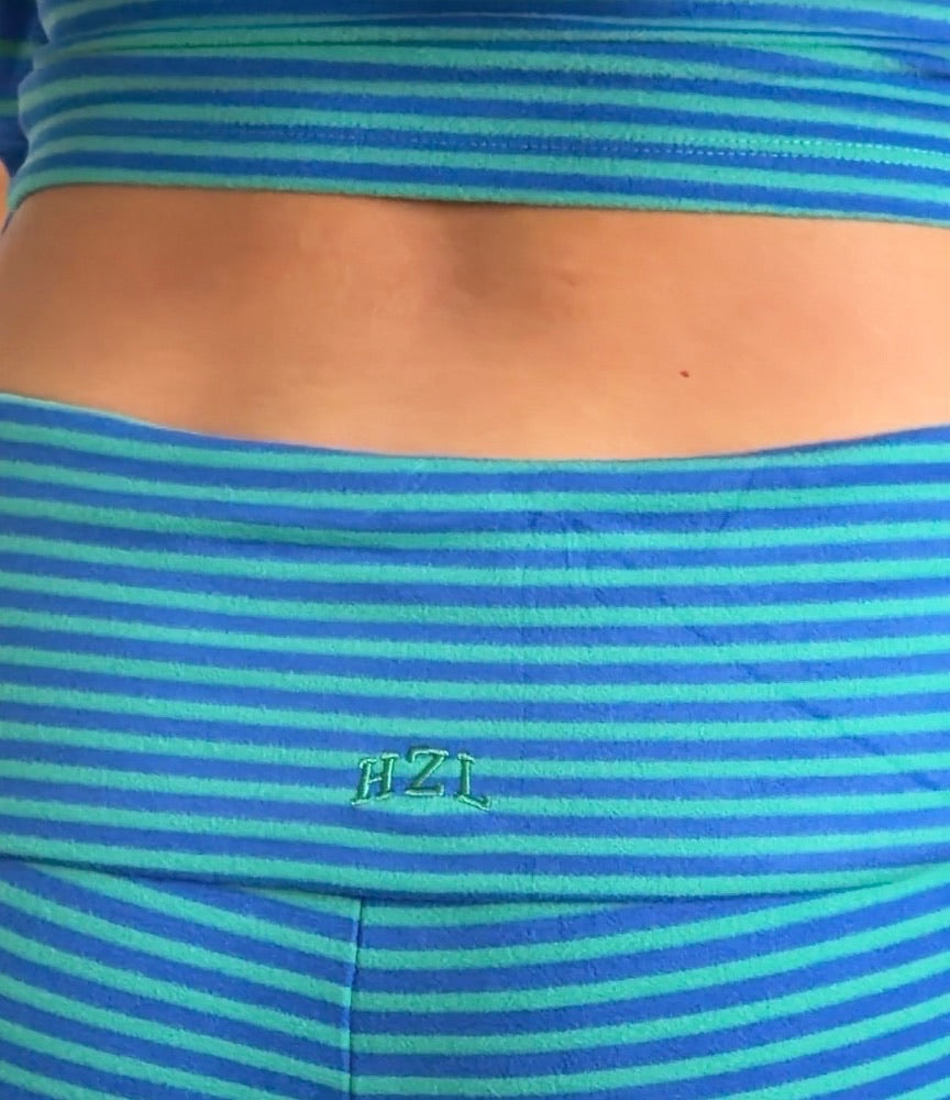 Close-up of a person wearing blue and green striped foldover shorts with a matching top, featuring subtle HZL embroidery.