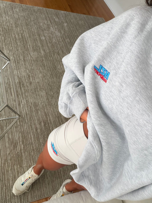 Close-up of a person wearing a grey sporty sweatshirt and white shorts with colorful logo details, casual look.