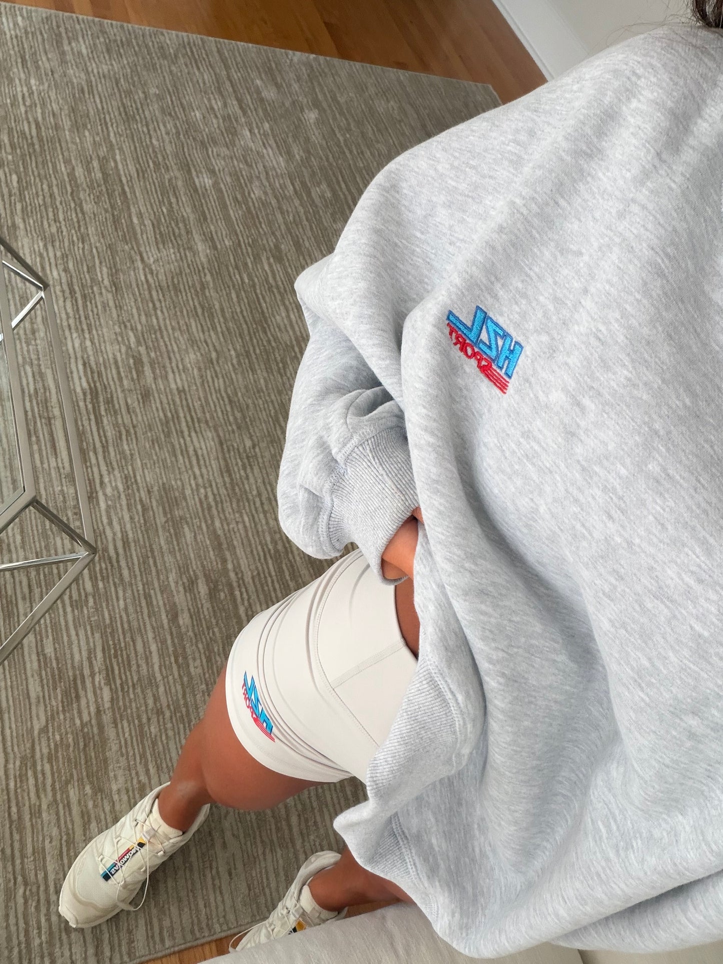 Close-up of a person wearing a grey sporty sweatshirt and white shorts with colorful logo details, casual look.