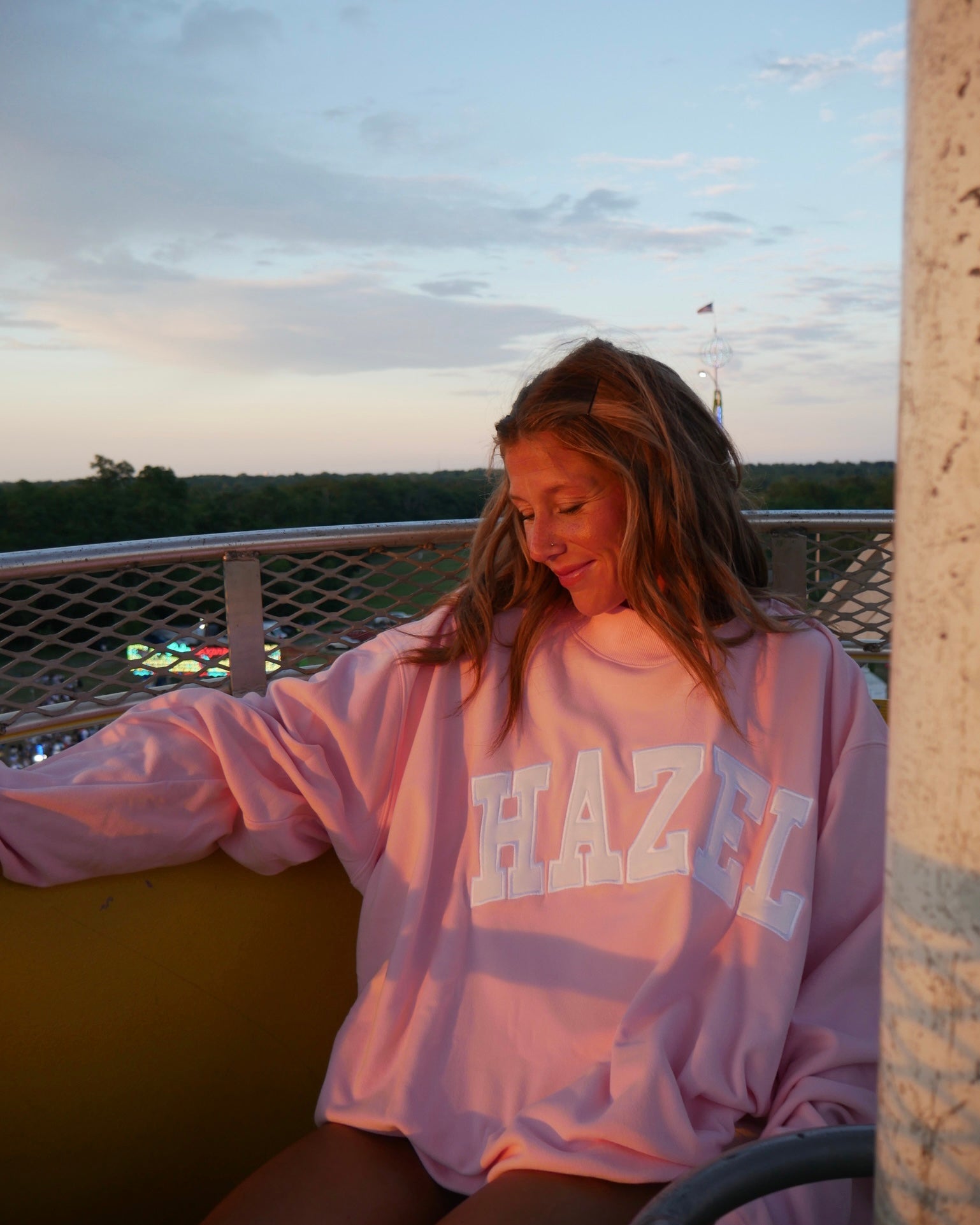 Young woman wearing a relaxed pink Hazel Boutique sweatshirt, enjoying a peaceful sunset outdoors.
