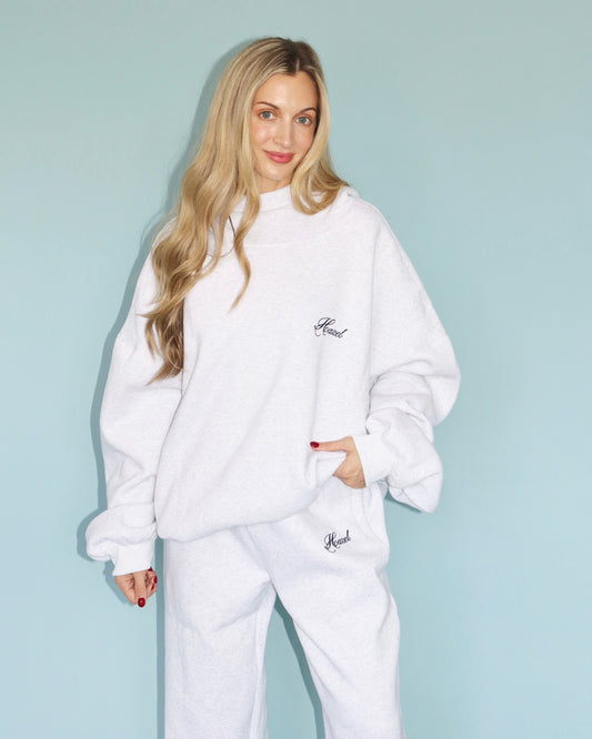 Woman wearing a white mockneck hoodie and matching sweatpants with small script logos