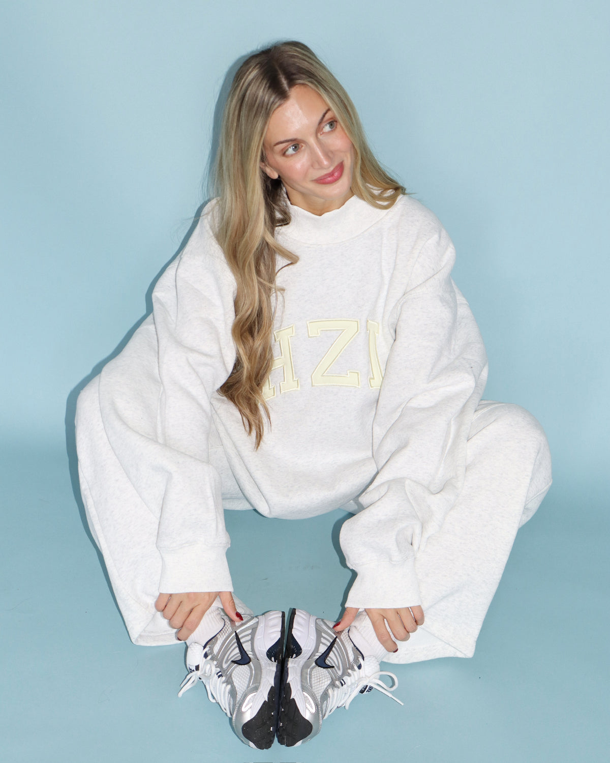 Woman wearing a white HZL mockneck sweatshirt with matching sweatpants and sneakers