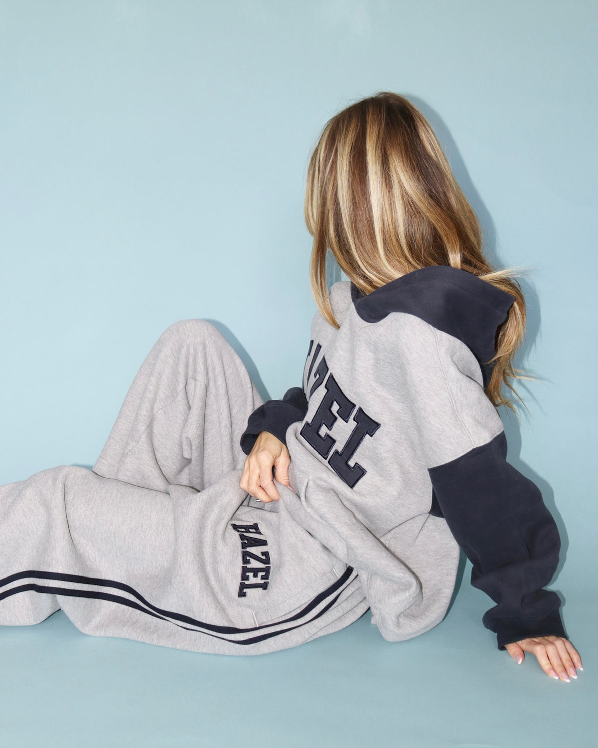 Model seated in gray HAZEL sweatpants with navy side stripes and a matching oversized sweatshirt