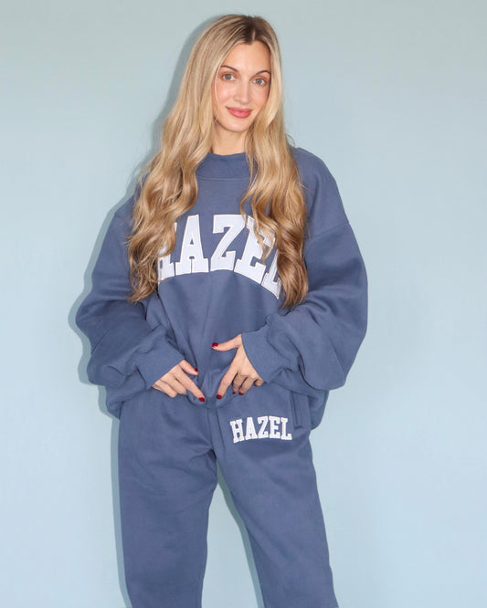 Model wearing a blue HZL mockneck sweatshirt and matching jogger pants with Hazel lettering