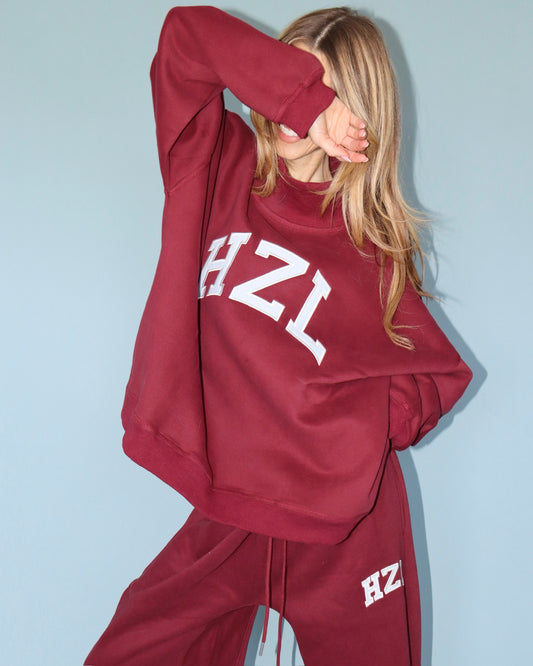 Model wearing a burgundy HZL sweatshirt and matching sweatpants with white lettering