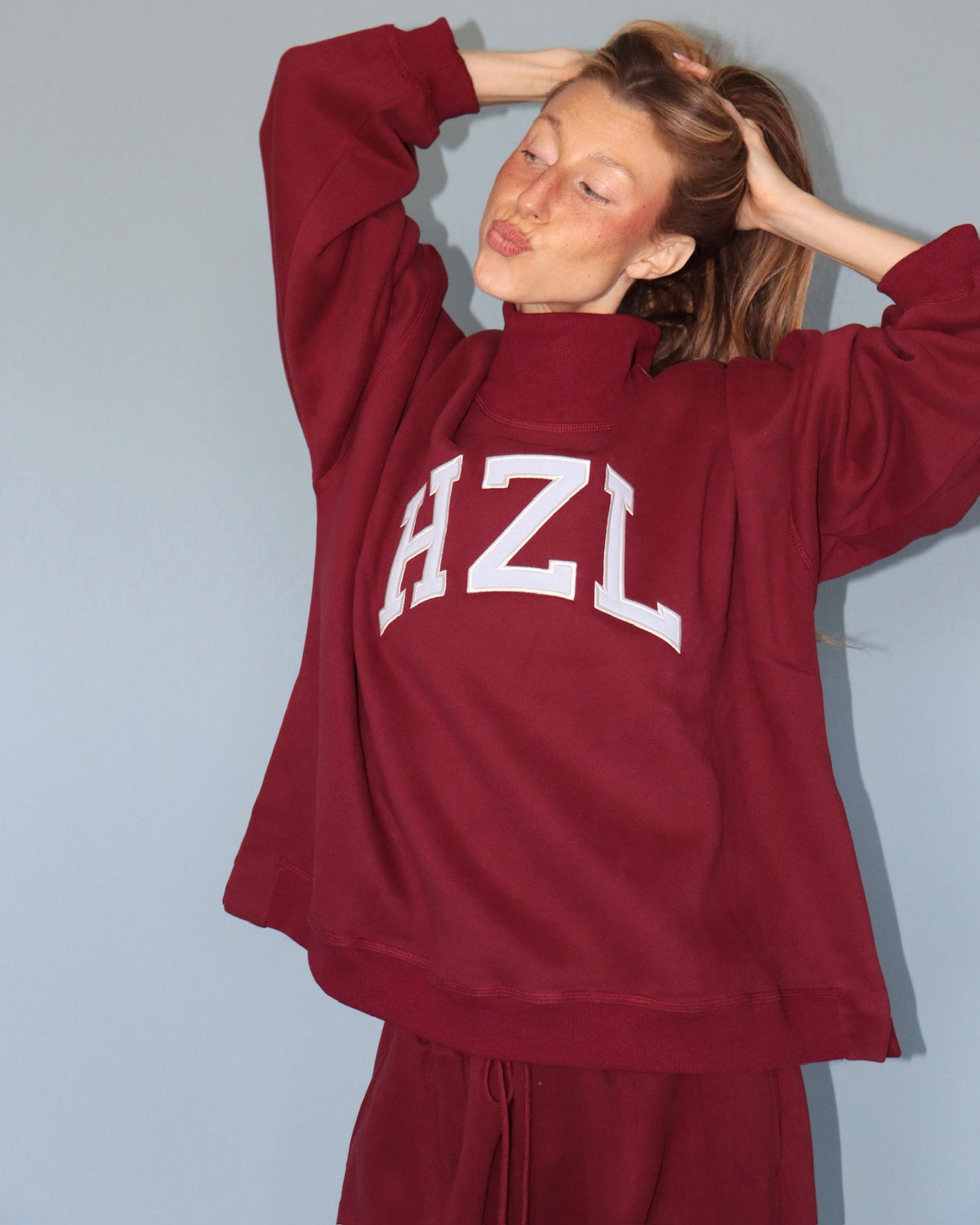 Woman wearing a burgundy HZL high neck sweatshirt with oversized sleeves and matching joggers